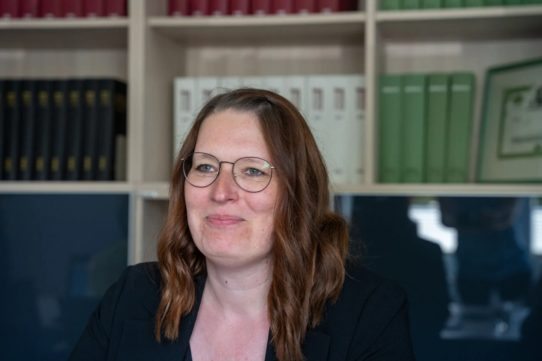 Frau mit langen Haaren sitzt vor einem Regal mit Ordnern