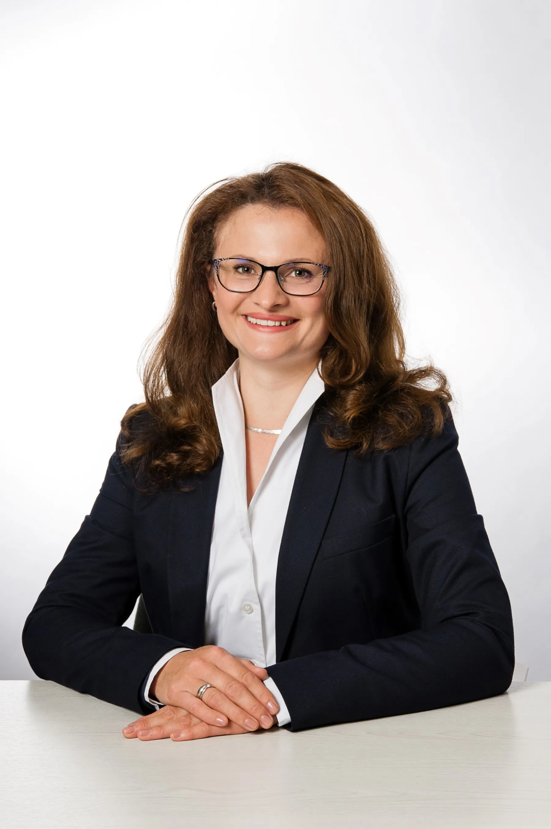 Frau mit lockigen Haaren im Business-Outfit an einem weißen Tisch.