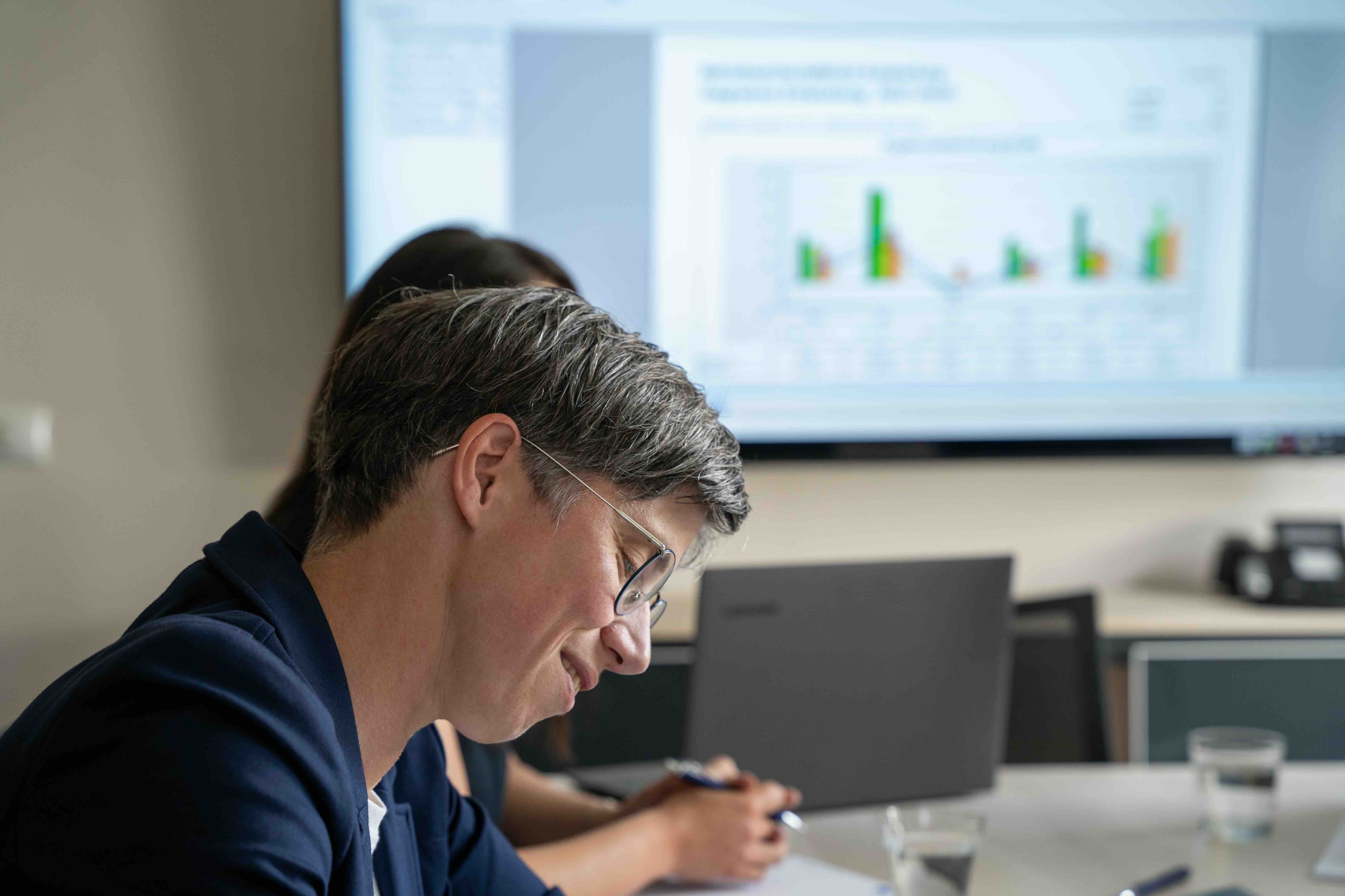 Person arbeitet, Bildschirm im Hintergrund zeigt Diagramme
