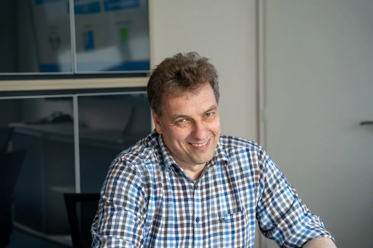 Mann mit kariertem Hemd sitzt an Schreibtisch
