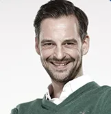 Mann mit grünem Pullover lächelt in die Kamera
